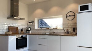 Et moderne køkken med hvide skabe, indbygget ovn, mikroovn og et vindue med udsigt til himlen.
