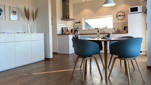 Et moderne køkken med spiseplads, der inkluderer en central ø, blå stole og en hængende lampe.