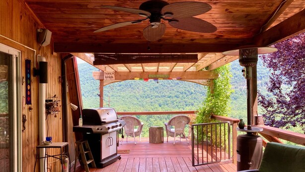 A wooden deck with a grill, chairs, and a view of a forested mountain. - Private mountaintop cabin with hot tub, pool table, and breathtaking views (Great Cacapon)