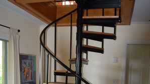 A spiral staircase with wooden steps and black metal railings in a room with a wooden floor, a door, and a window with curtains. - Private mountaintop cabin with hot tub, pool table, and breathtaking views (Great Cacapon)