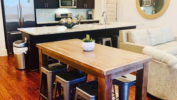 A modern kitchen with dark cabinets, stainless steel appliances, a central island with stools, and a white sofa in the living area. - The Seahorse 30A! Golf Cart Included! Sleeps 10! (Santa Rosa Beach)