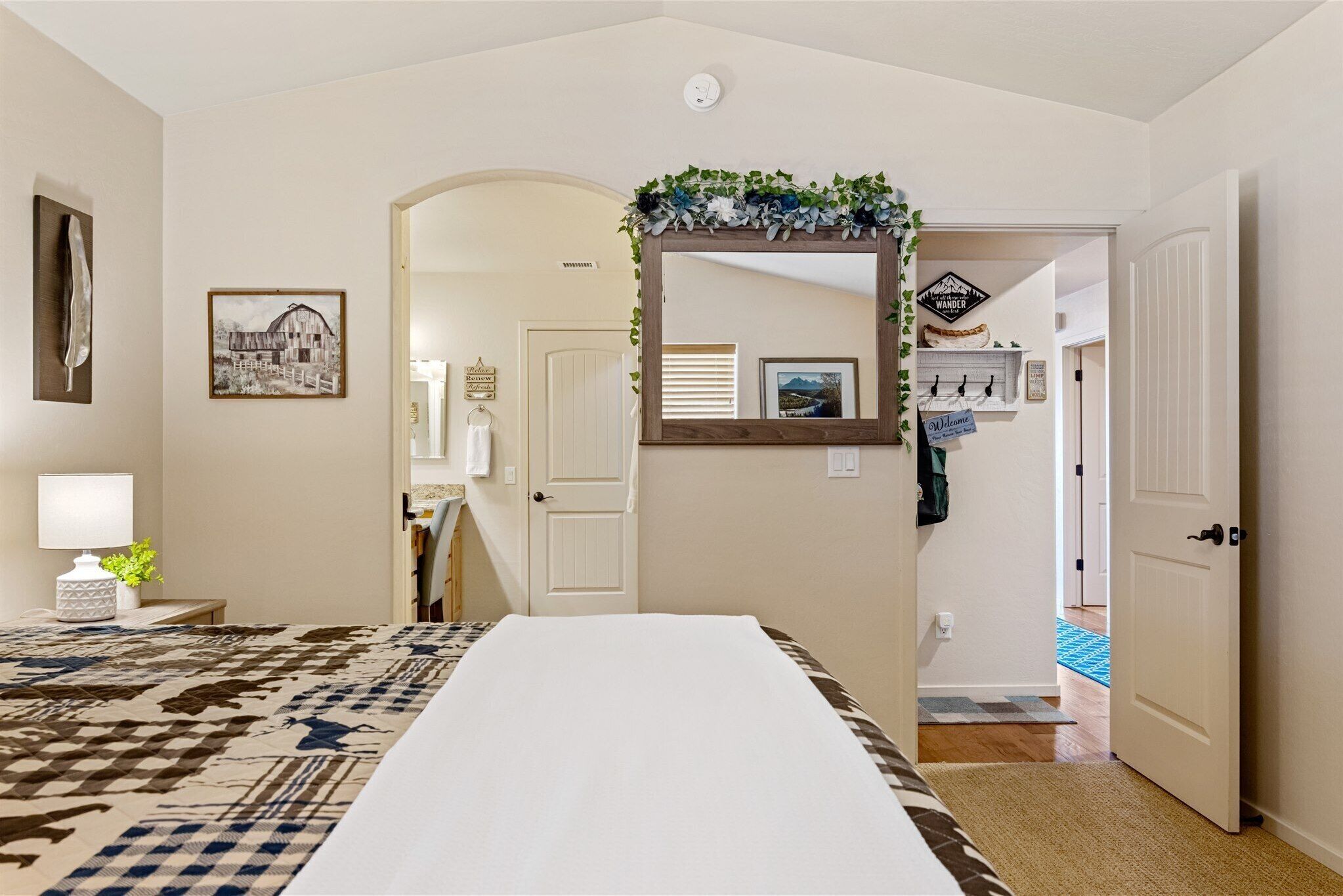 A hotel room with a large bed, a mirror with a decorative frame, a wall-mounted picture, and a door leading to another room.