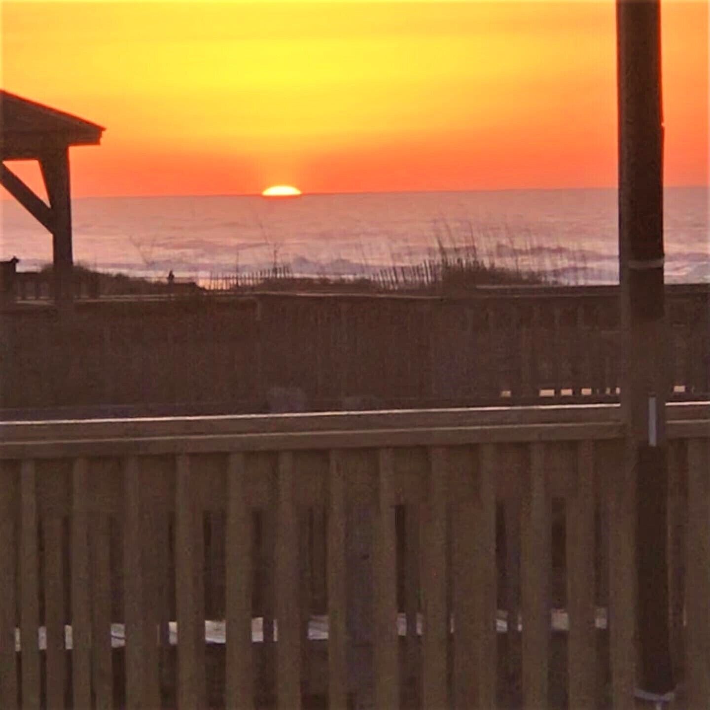 Een houten steiger die zich uitstrekt over de oceaan, met een zonsondergang op de achtergrond.