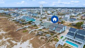 An aerial view of a coastal residential area with houses, a water tower, and a swimming pool.
