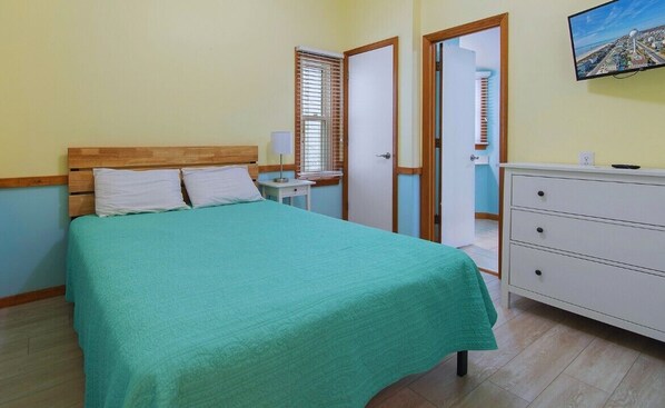 A bedroom with a bed, bedside table, dresser, and a television on the wall. - Wide Ocean Front, Private Gazebo, 6 Bedrooms, New to VRBO (Ocean Isle Beach)