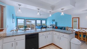 A kitchen with white cabinets, granite countertops, and a dishwasher. There is a dining area with a table and chairs.