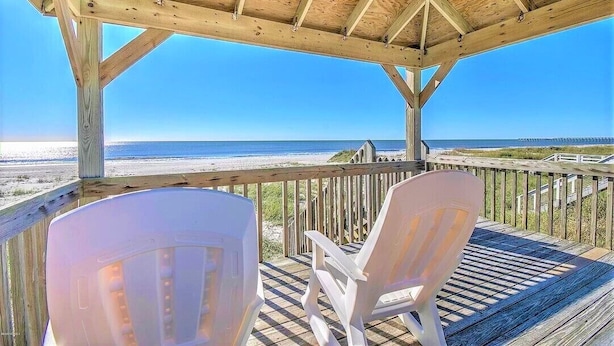 A wooden deck with two white chairs overlooking a beach.