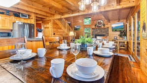 Interior de una cabaña de madera con una mesa de comedor para cuatro, armarios de madera, una zona de cocina y una escalera.