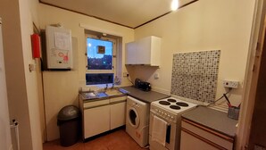 Uma cozinha compacta com máquina de lavar, fogão, pia e janela com vista para a cidade.