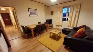 Uma sala de estar com sofá, mesa de centro, televisão e uma área de jantar com cadeiras e mesa.