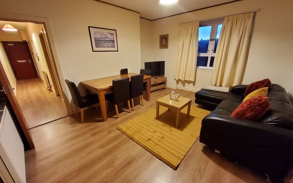A living room with a sofa, a coffee table, a TV, and a dining area with chairs and a table.