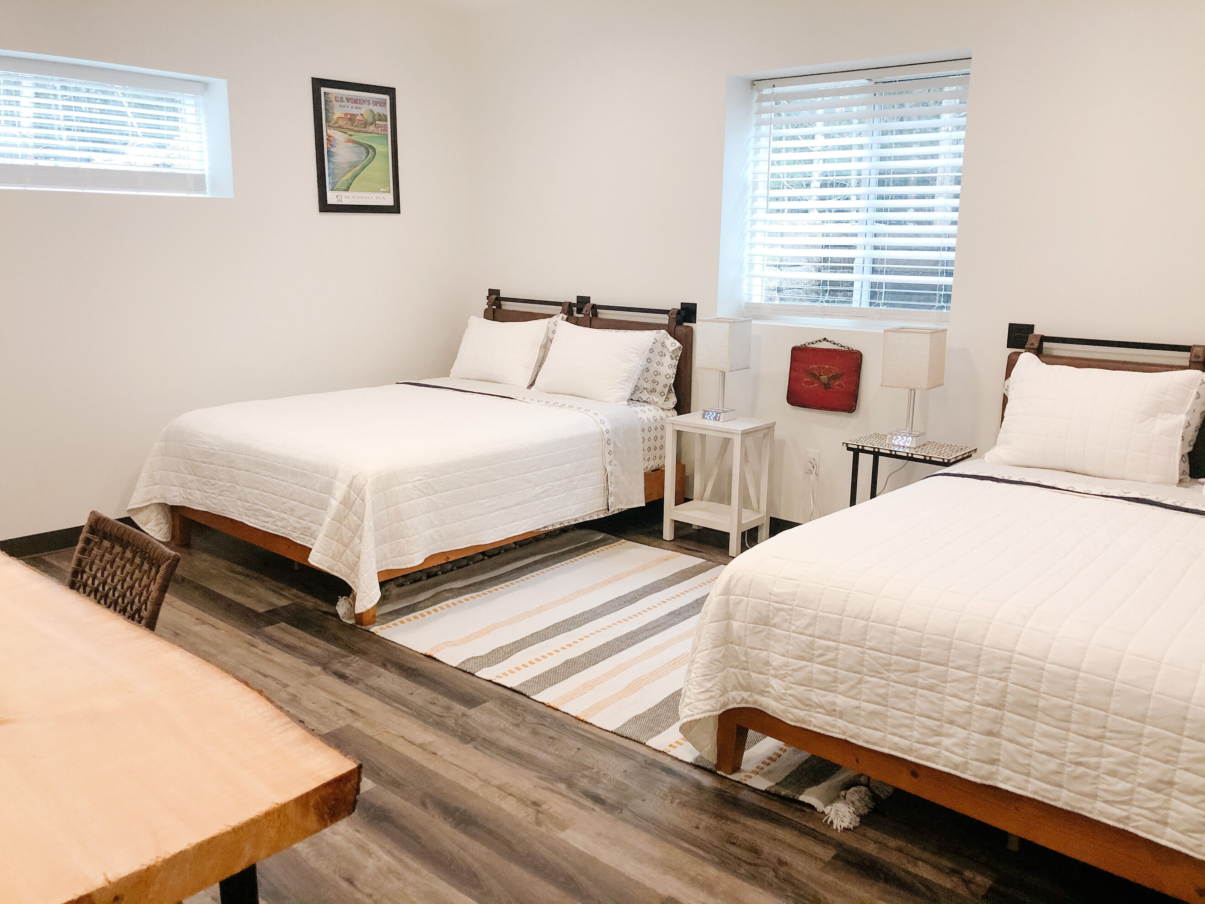 A hotel room with two beds, a small table, and a window with blinds.