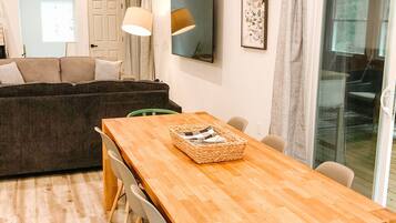 A modern living room with a wooden dining table, a sofa, and a large window.