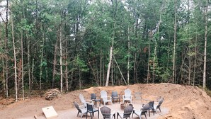 An outdoor seating area with chairs and tables arranged on a gravel surface, surrounded by a forest. - Eagle's Nest Guest House II - Less than 2 Miles to Sand Valley - 16 beds! (Nekoosa)