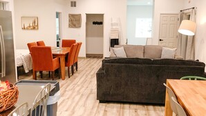 A spacious living area with a wooden dining table, orange chairs, a dark grey sofa, and a white ceiling fan. - Eagle's Nest Guest House II - Less than 2 Miles to Sand Valley - 16 beds! (Nekoosa)