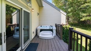 Una terraza con un jacuzzi, una puerta corredera de vidrio y barandilla de madera.