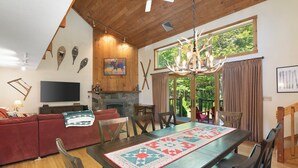 Un salón acogedor con chimenea, techo de madera y un gran ventanal con cortinas.