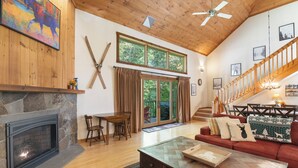 Amplia sala de estar con chimenea de piedra, techo de madera y una escalera que sube a un nivel superior.