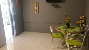 A dining area with a round table, green chairs, and a TV mounted on the wall. - Studio for rent (Case-pilote)