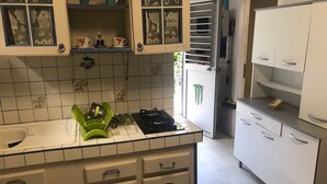 A kitchen with white cabinets, a green dish rack, a stove, and a refrigerator. - Studio for rent (Case-pilote)