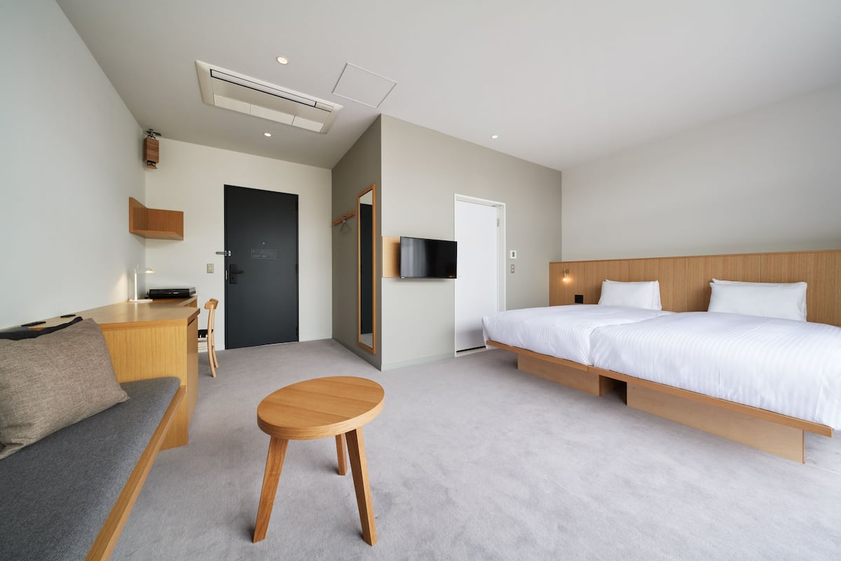 A modern hotel room with a bed, a sofa, a small table, a desk, a TV, and a door.