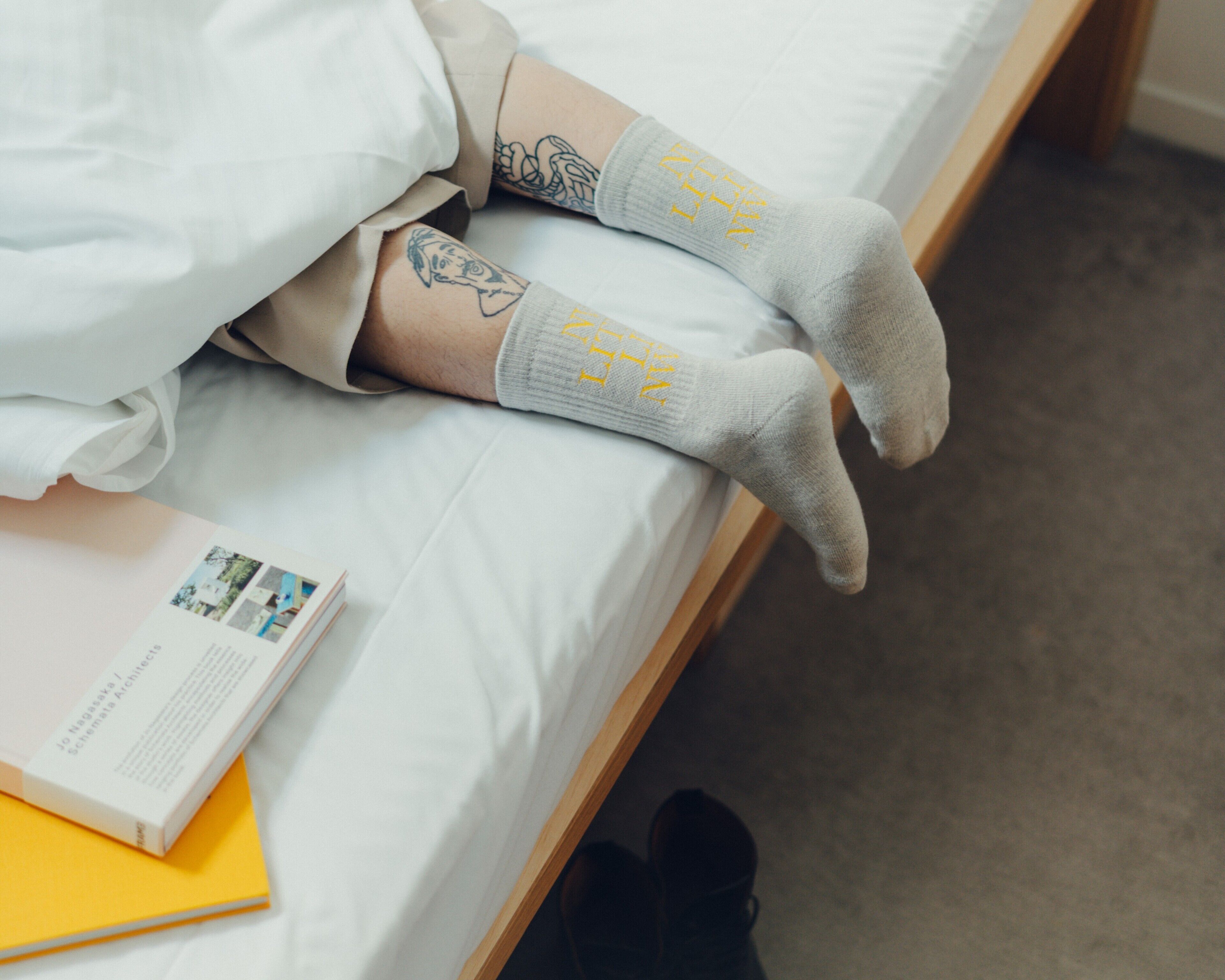 Eine Person liegt im Bett mit einem Buch und einer gelben Ordner daneben.