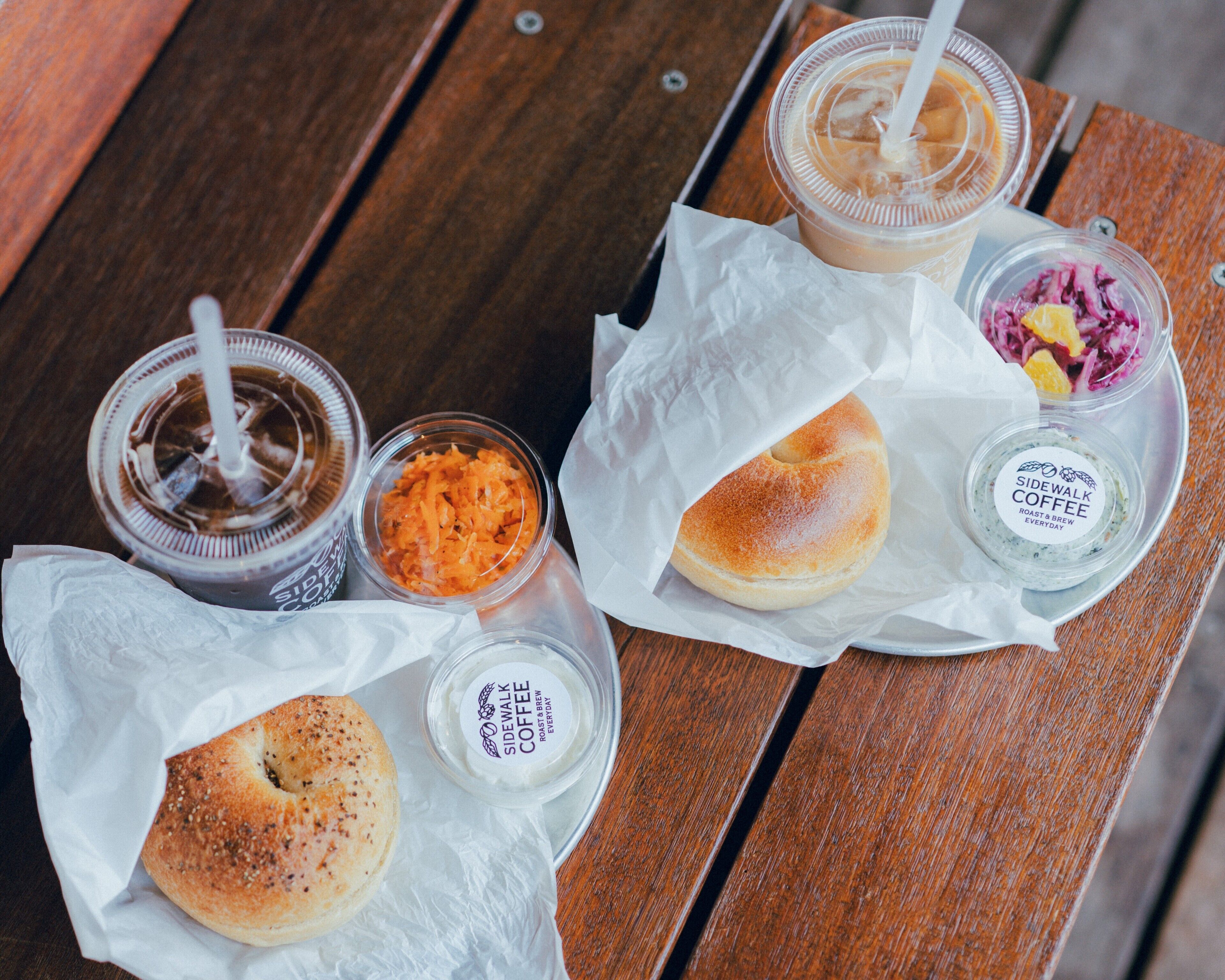 A meal with a bagel, coffee, and coleslaw on a wooden table.