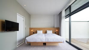 A modern bedroom with a large bed, a flat-screen TV mounted on the wall, and a large window offering a view of the outdoors.