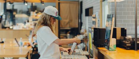 A person at a coffee and bagel counter in a cafe with a visible menu and a coffee machine.