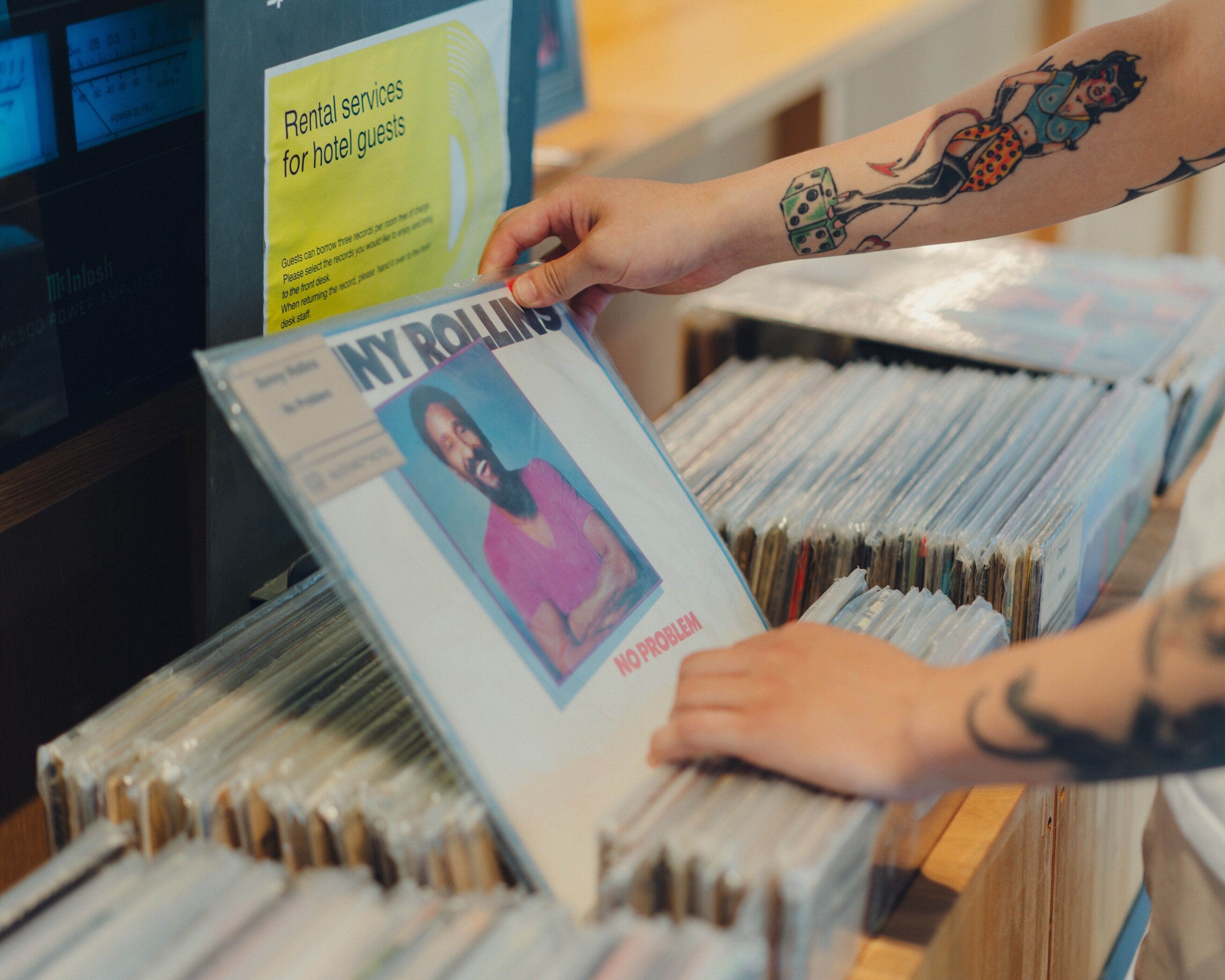 A person browsing through a collection of magazines or books, with a sign indicating rental services for hotel guests.