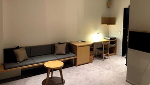 A modern living room with a sofa, a small round table, a desk with a lamp, and a cabinet.