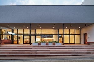A modern building with a glass facade, wooden steps leading to the entrance, and outdoor seating.