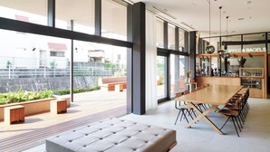 A modern dining area with a long wooden table, cushioned seating, and a view of the outdoors through large windows.
