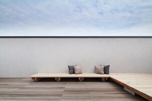 A minimalist room with a wooden platform bed, two pillows, and a plain wall.