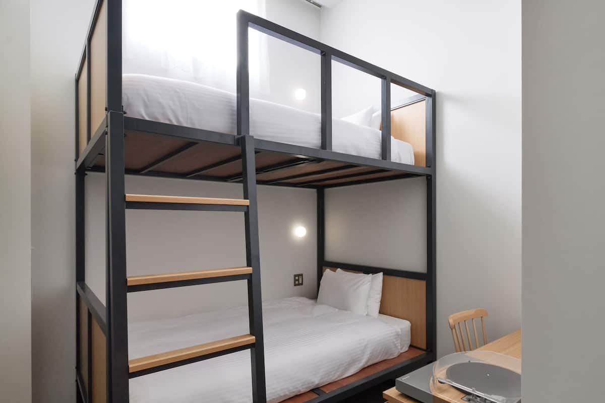 A bunk bed with a desk and chair, a small cabinet, and a light fixture on the wall.