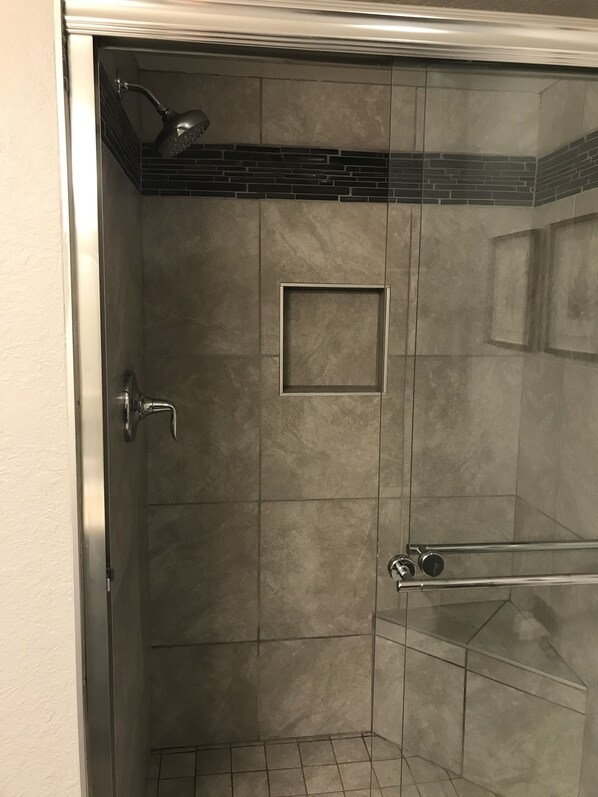 Un box de ducha con paredes de vidrio, suelo de baldosas y una pequeña ventana cuadrada.