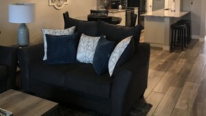 Ein modernes Wohnzimmer mit einem schwarzen Sofa, einem Couchtisch und einem Essbereich mit einer Chandelier.