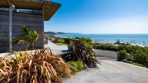 A modern building with a sloped roof and solar panels, overlooking a coastal area with a clear view of the ocean. - Bach or holiday home, 1 Bedrooms, 2 Bathrooms, (Sleeps 2) (Waimarama)
