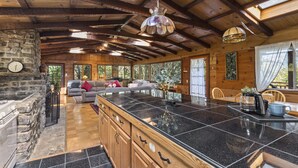 A spacious kitchen with a large island, wooden beams on the ceiling, and a stone wall. - Spacious Serene Sanctuary-Minutes to SF and Muir Woods (Mill Valley)