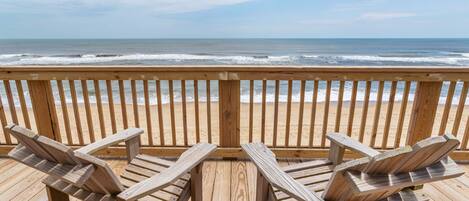 A wooden deck with two Adirondack chairs facing a beach with ocean waves.