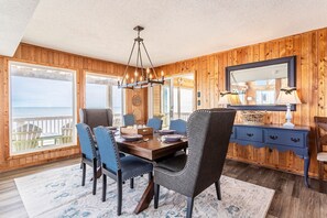A dining area with a wooden interior, a large window overlooking the sea, and a chandelier. - Sunrises, Sunsets☀️Hot Tub, Shared Pool, Beach Chairs, Oceanfront, SUMMER SALE (Avon)