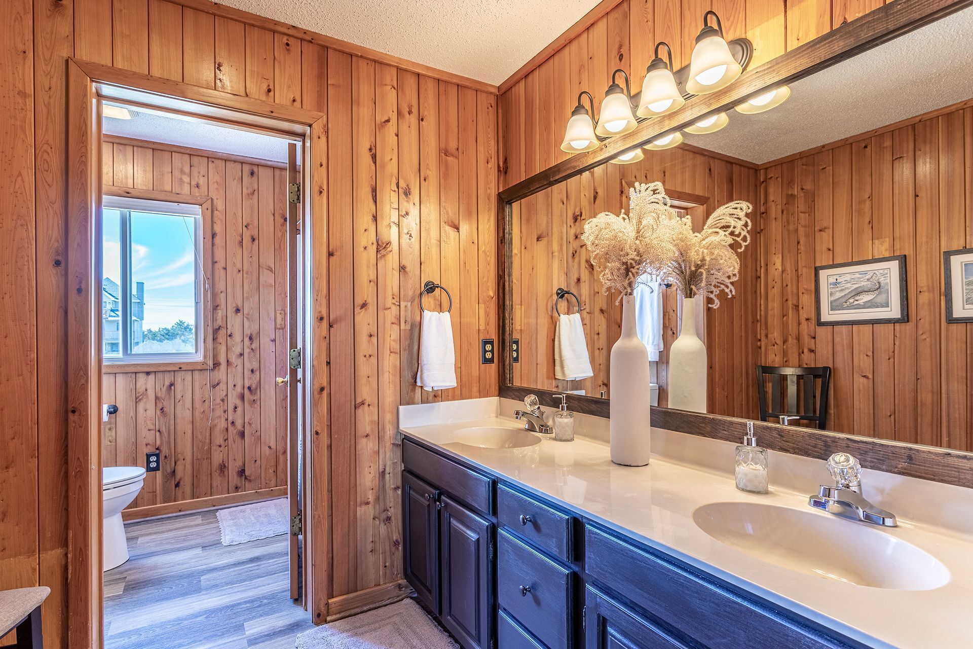 A wooden-paneled bathroom with a large mirror, two sinks, and a window.