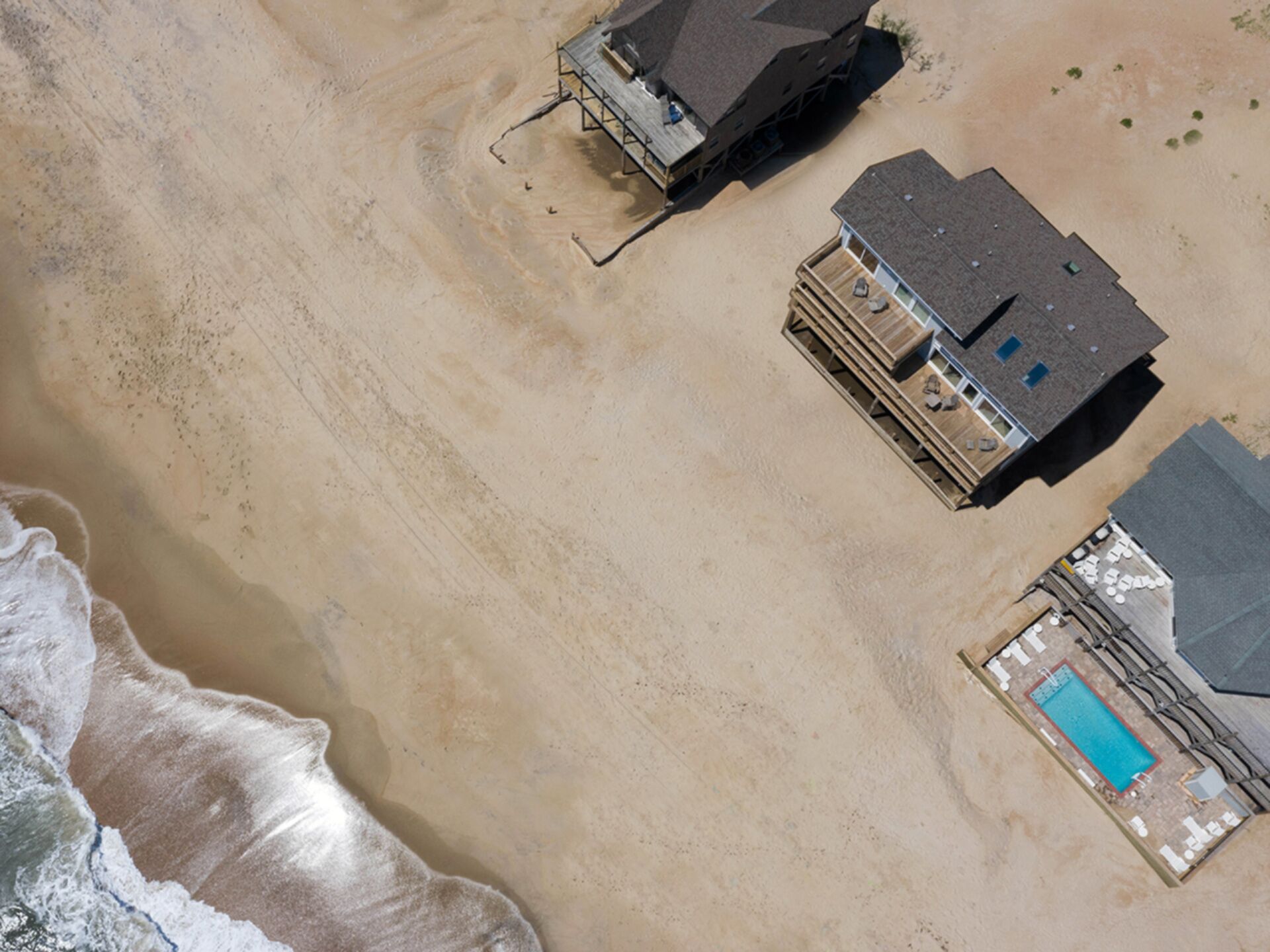 An aerial view of a beachfront property with a large house, a smaller building, and a swimming pool.