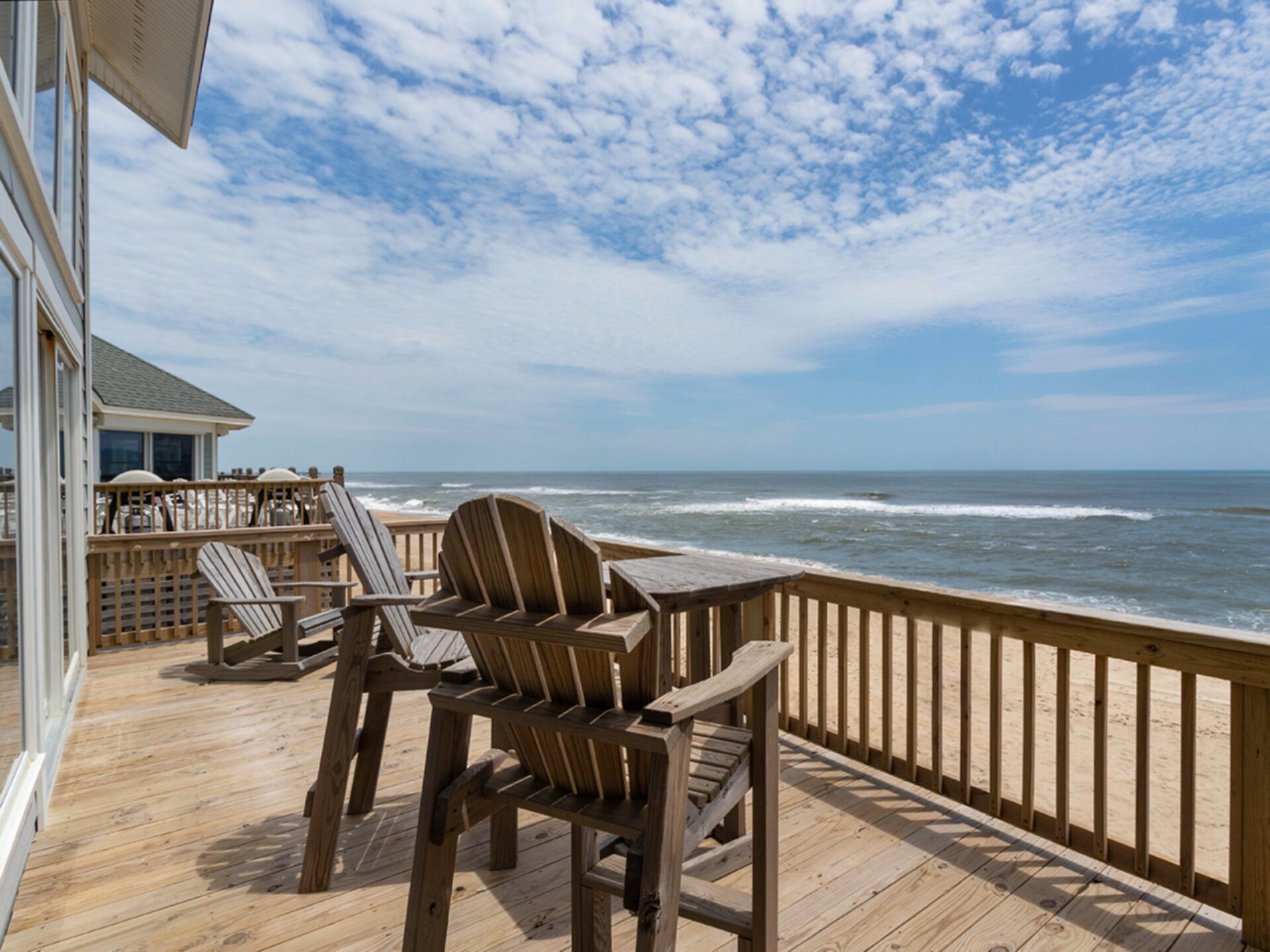 A wooden deck with Adirondack chairs overlooking the ocean.