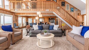 A spacious loft-style living area with a high ceiling, wooden walls, and a balcony overlooking the ocean.