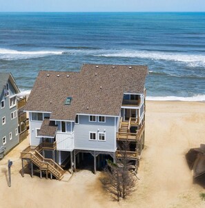 A beachfront multi-story house with a balcony, a staircase leading to the beach, and a sandy area in front. - Sunrises, Sunsets☀️Hot Tub, Shared Pool, Beach Chairs, Oceanfront, SUMMER SALE (Avon)