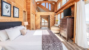 A spacious bedroom with a large bed, a dresser, a television, and a ceiling fan.