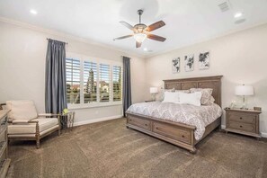 A bedroom with a large bed, a ceiling fan, a nightstand, a chair, and a window with curtains. - Ritz Waters at Ocotillo, Heated Pool, 5br/3.5 bath (Chandler)