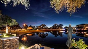 Une vue nocturne d’un espace piscine extérieur paisible, avec une statue, des chaises longues et un chemin éclairé.