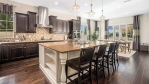Une cuisine moderne avec des meubles de couleur sombre, un grand îlot central et des luminaires suspendus.